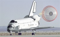 The Space Shuttle Atlantis lands with its drag chute deployed on runway 22 at Edwards, California, to complete the STS-66 mission.